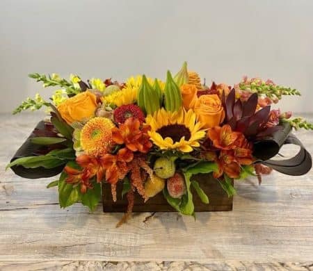 This festive autumnal arrangement of golden sunflowers burst from a charming wood box, with roses, orange alstrolilies, bronze amaranthus, yellow and orange snapdragon with decorative fruit is sure to delight!