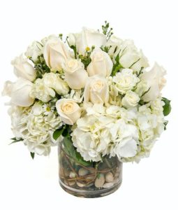 This striking array of white roses and hydrangea handcrafted in a round glass vase is sure to bring elegance to any room and occasion.