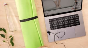 Wooden floor, green yoga mat, clear water bottle, and virtual yoga class on open laptop